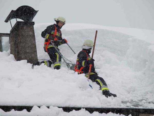 Zwei Feuerwehrmänner beim Abschaufeln eines Hausdaches