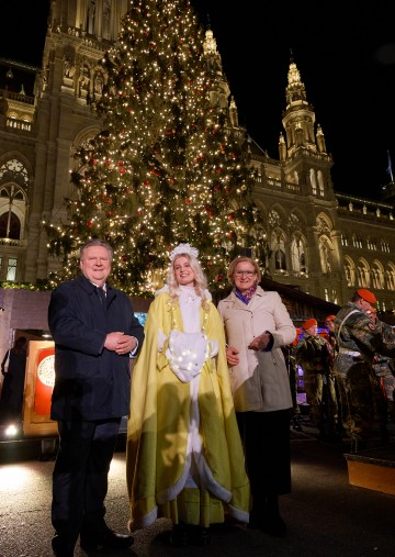 Bürgermeister Michael Ludwig, Christkind Lena und Landeshauptfrau Johanna Mikl-Leitner vor dem Christbaum am Wiener Rathausplatz (v.l.n.r.).